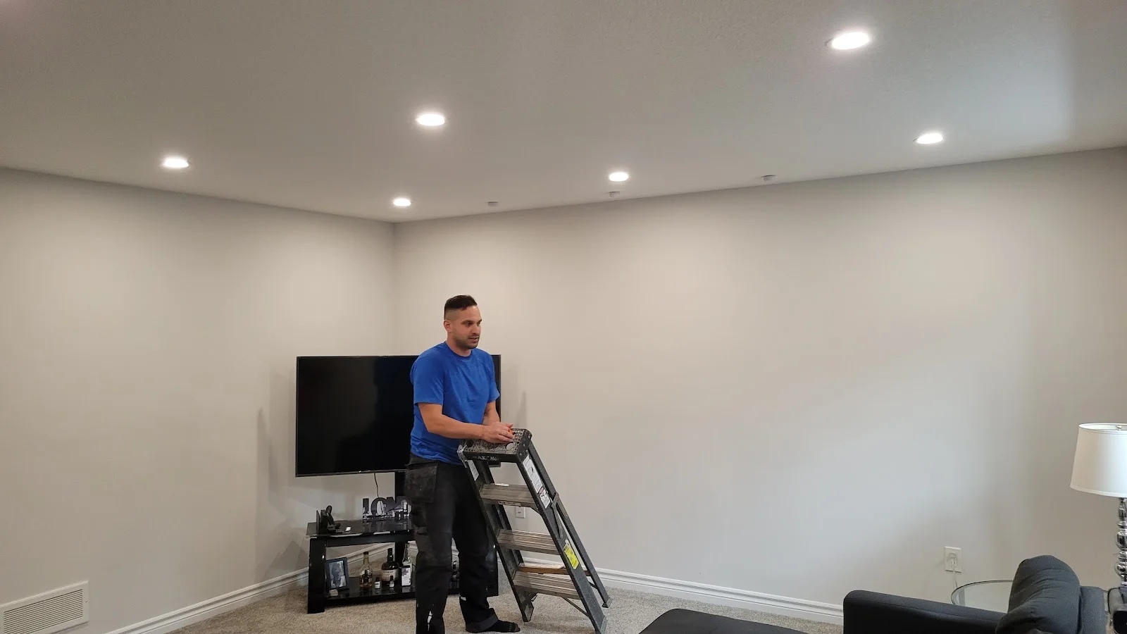 A Boost Electric team member on a step ladder installing recessed pot lights in a living room